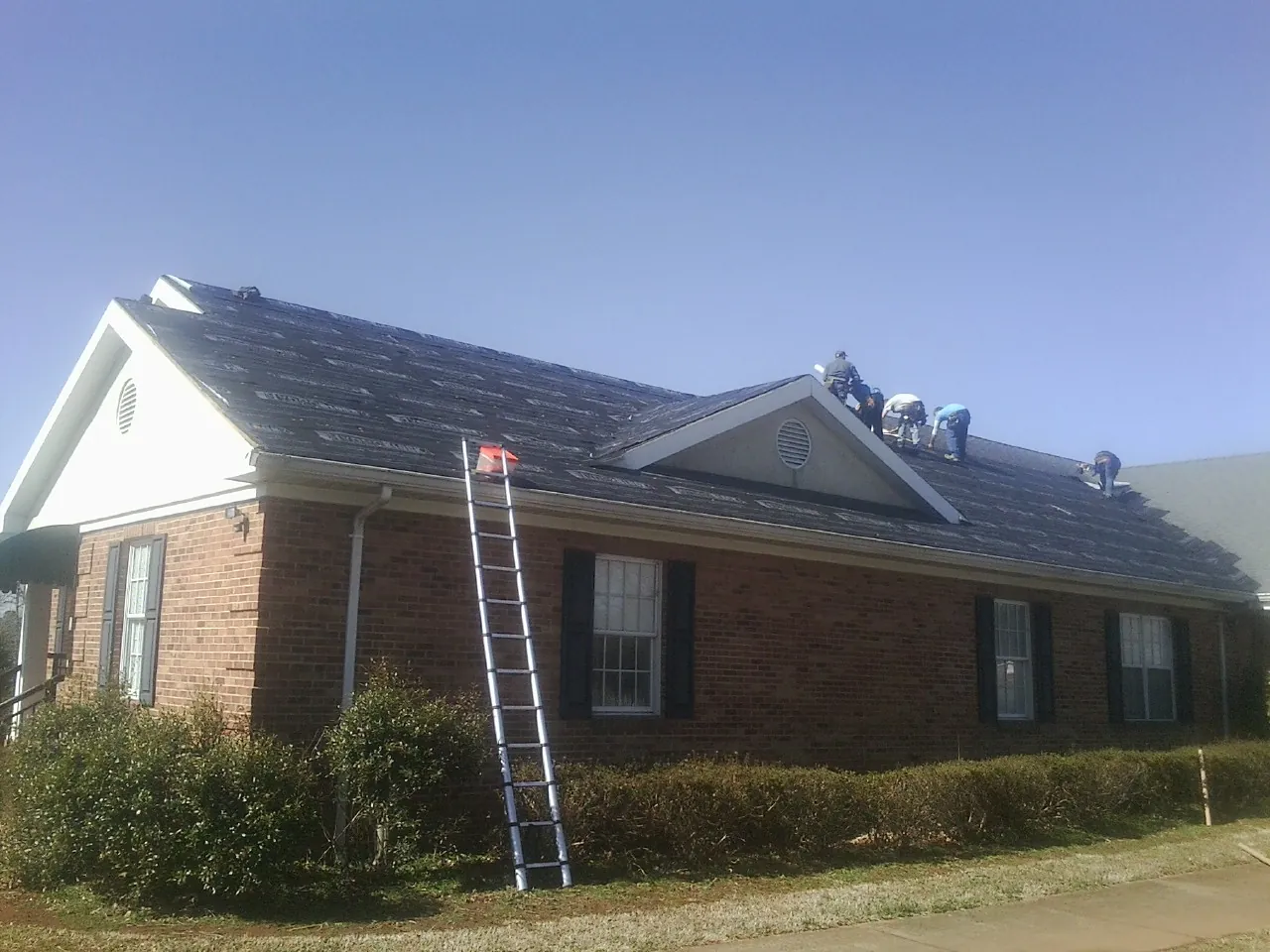 Crew tearing shingles off a brick ranch roof with a ladder set — Metal Roof Repair work by our crew in Lumberton