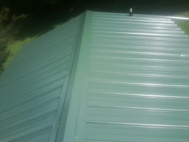 New green metal panels meeting at the ridge of a roof — Flat Roof Repair work by our crew in Lumberton
